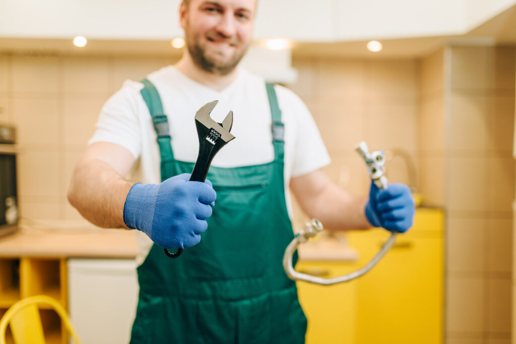 Plumber in uniform holds wrench, handyman. Professional worker makes repairs around the house, home repairing service